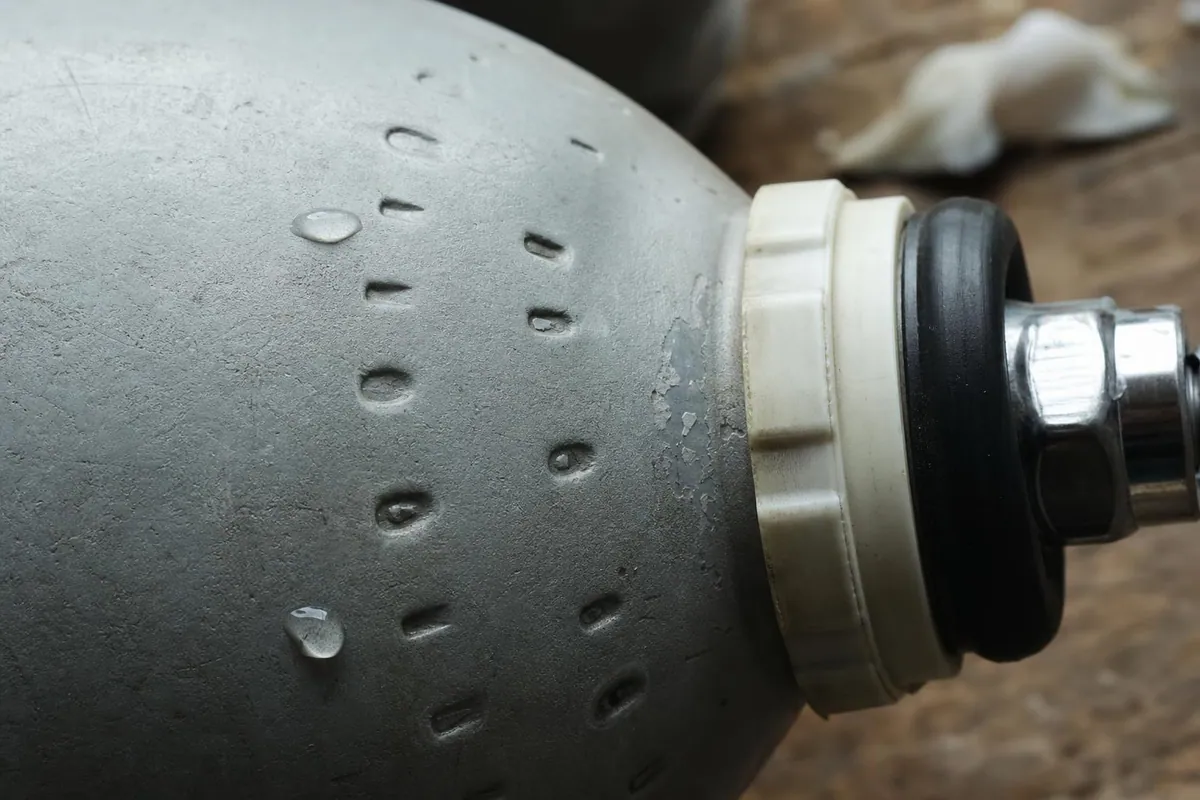 Gros plan macro sur l’ogive d’un bloc de plongée en acier peint, montrant les poinçons gravés de pression et de date ainsi qu’un collier d’identification en plastique